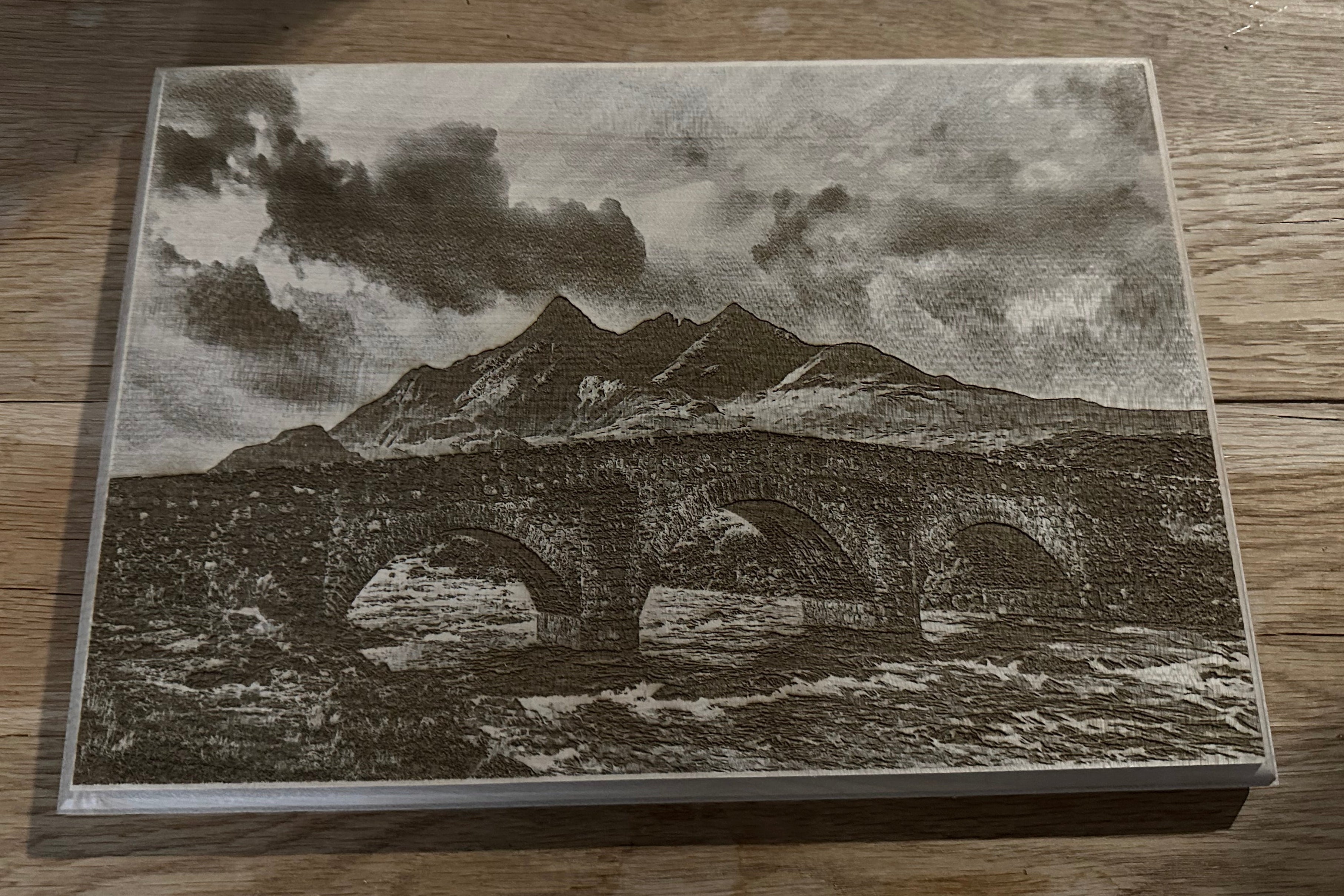 Wooden plaque with a mountain and bridge design on a wooden surface